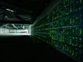 Bitcoin mining machines in a dark hangar, with small green lights.