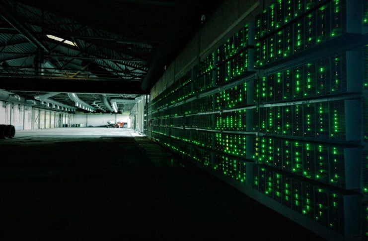 Bitcoin mining machines in a dark hangar, with small green lights.