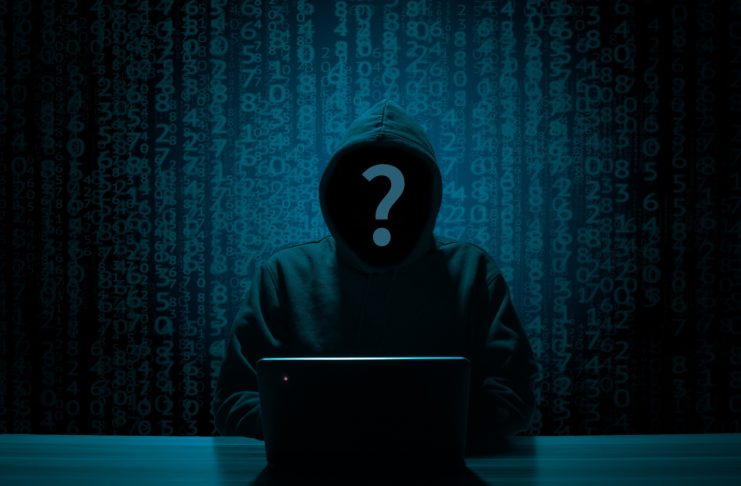 Hacker sitting in front of a laptop, while numbers appear behind him.