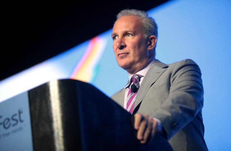 Peter Schiff speaking to the audience behind a desk, wearing a suit and a purple tie.