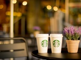 Two starbucks coffee cup on a table, next to a lavender in a flowerpot.