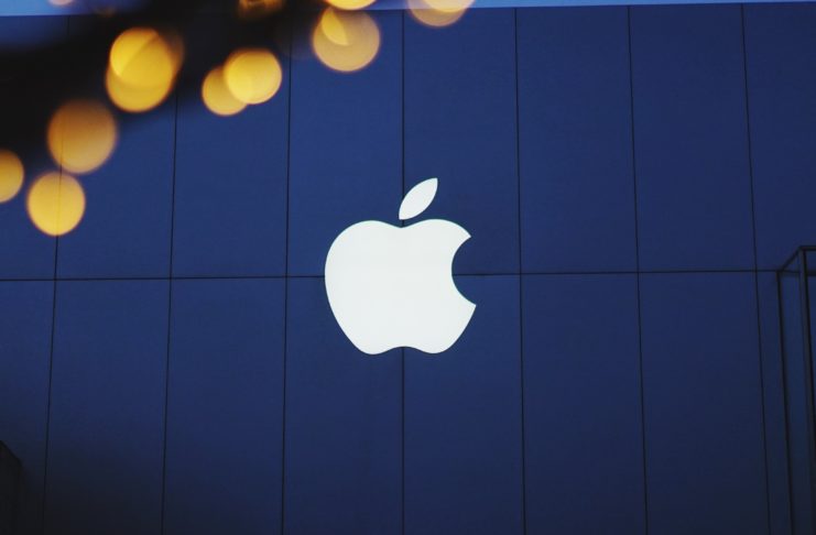 White Apple logo on a blue building, with yellow lights at top.